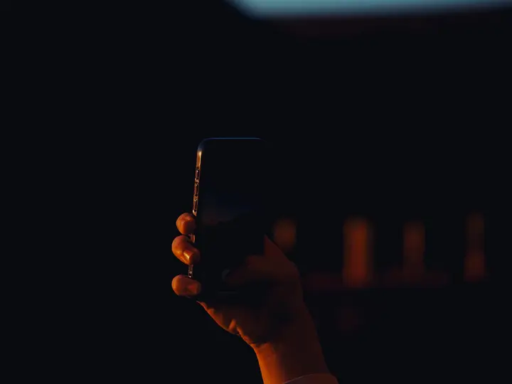 Mano sosteniendo un teléfono encendido sobre un fondo oscuro